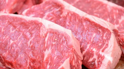 Several raw, marbled beef steaks are arranged closely together on a wooden surface.