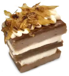 A layered slice of brown and white Happy Cakes for Cats, topped with a dollop of white cream and shredded dried fish flakes.