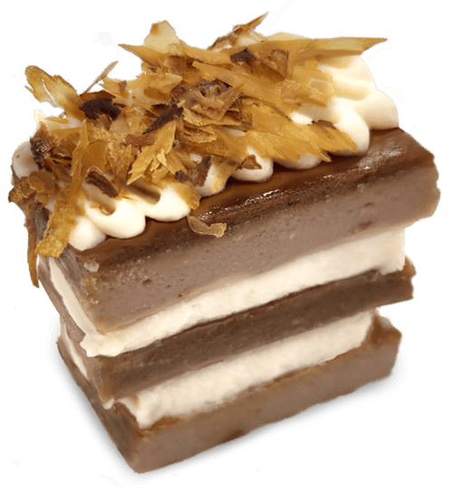 A layered slice of brown and white Happy Cakes for Cats, topped with a dollop of white cream and shredded dried fish flakes.