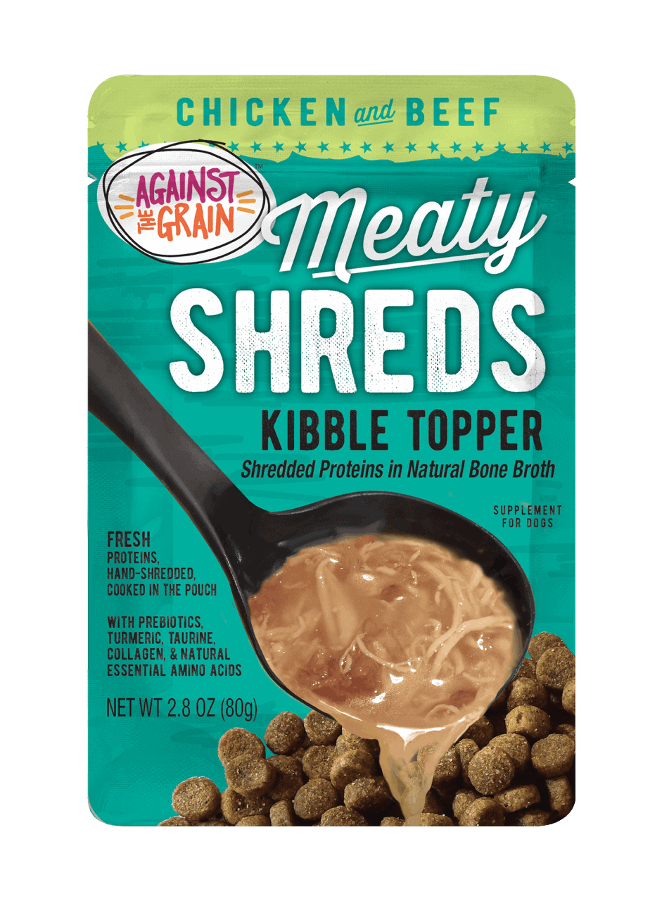 A pouch of Shreds Slow Cooked Shredded Chicken & Beef Kibble Topper is shown with a spoon over dry dog food.